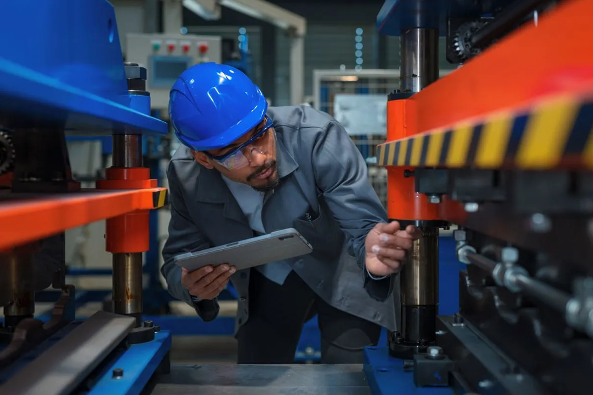 Ein Techniker mit blauem Helm und Tablet beugt sich prüfend über eine Werkzeugmaschine