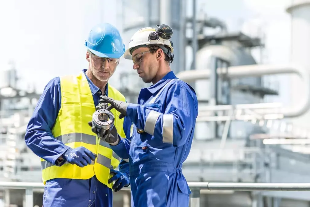 Zwei Techniker in Arbeitskleidung begutachten gemeinsam ein ausgebautes Lager vor einer Industrieanlage